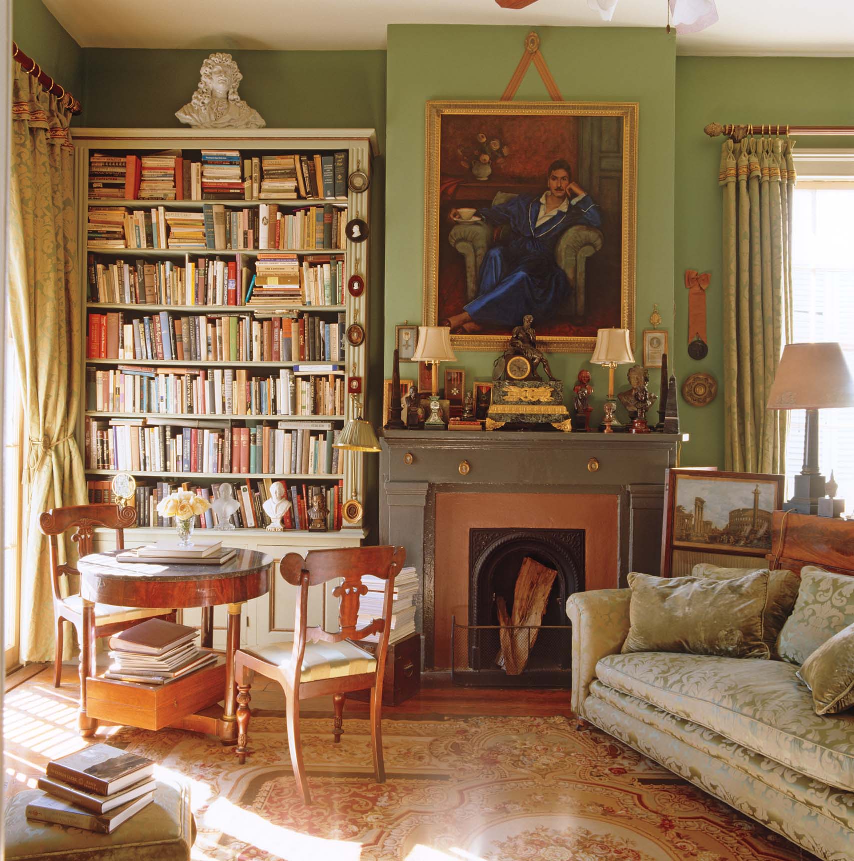 Patrick Dunne's home library is painted a soft green and is filled with sunlight by tall windows. A portrait hanging above the fireplace in the living room sets the tone for the library corner where a Biedermeier table and chairs provide a sunlit place to read