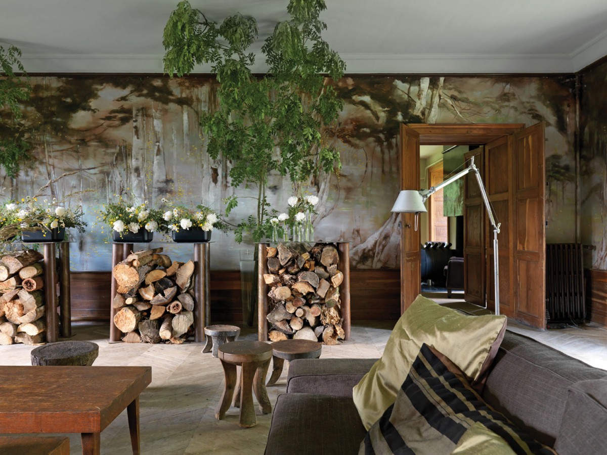 Claire Basler's salon features a woodlands mural that ensconces the room in natural hues. Stacks of fire wood stored under a trio of high tables echo the theme.