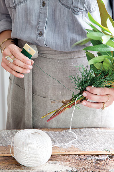 Jessica Sloane wraps twine around a bundle of evergreen branches and berries for her garland