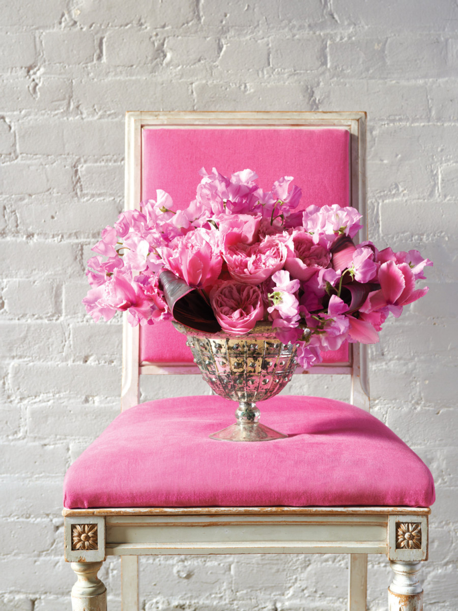 Think pink arrangement in silver footed vessel on pink upholstered dining chair.