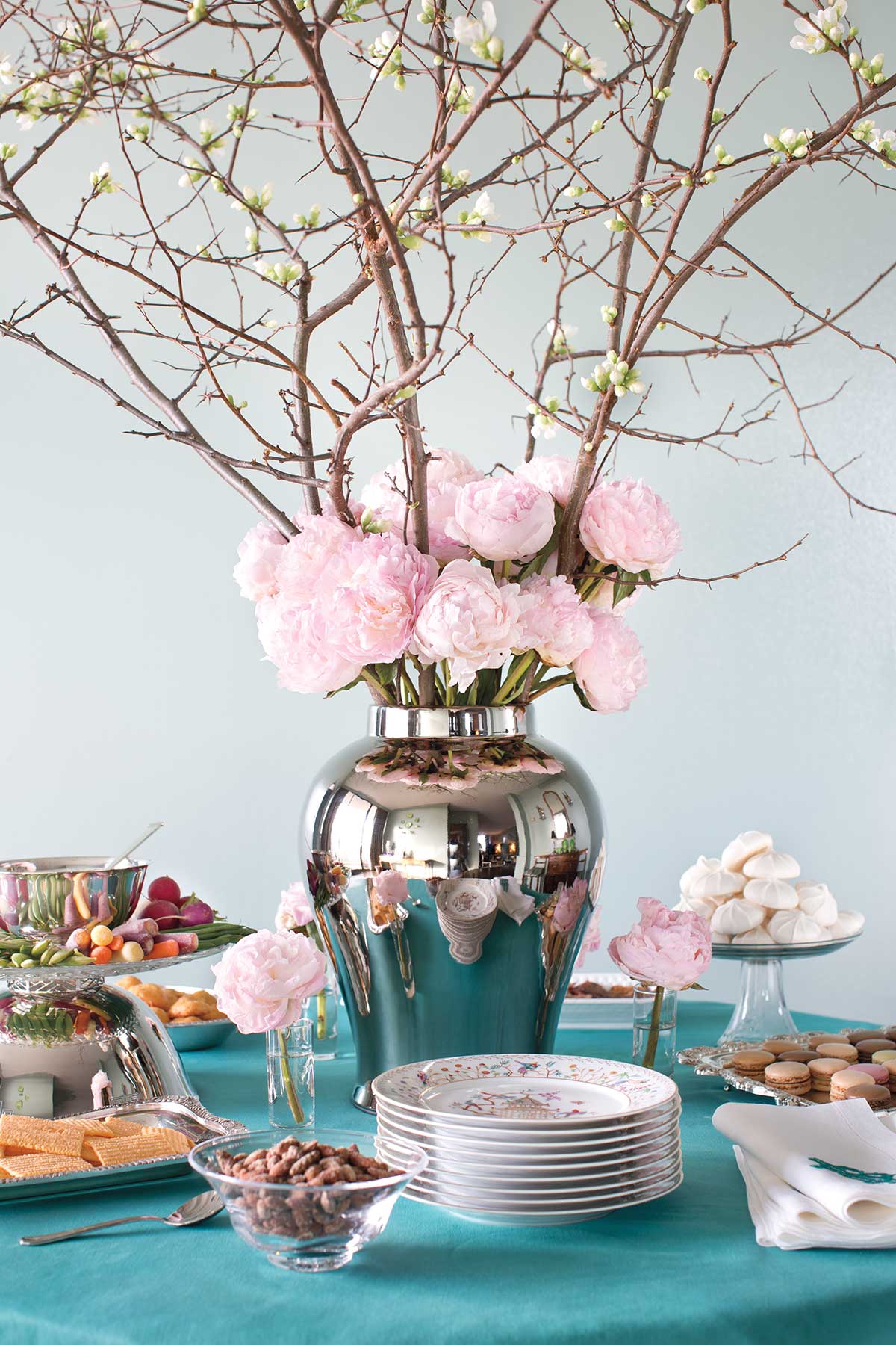 A tangle of quince with frothy pink peonies and shot glasses with single peony blossoms anchor a table set with hors d'oeuvres at this Jennifer Boles cocktail party.
