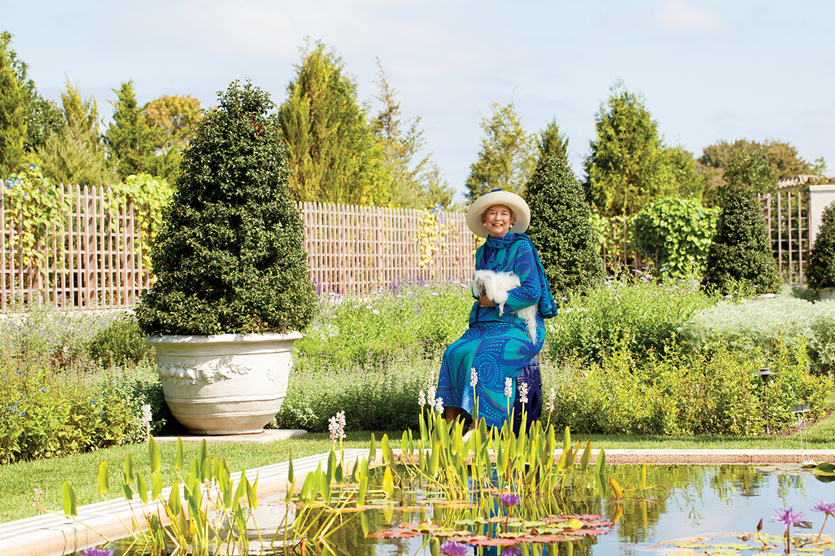 A modern-day (2016) portrait of philanthropist/horticulturist Dorrance "Dodo" Hamilton, wearing a blue dress and sitting by a garden pool in the Blue Garden, mirroring a classic portrait of the garden's original owner.
