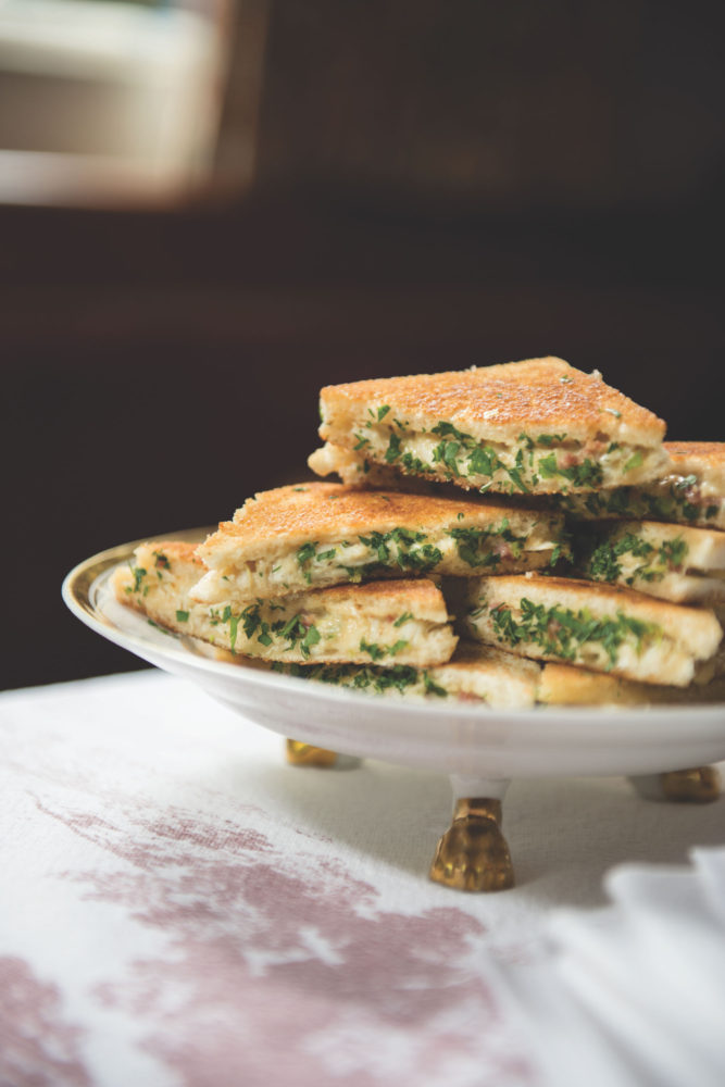 Deviled crab and cheese sandwiches, cut diagonally, on a footed, gold-rimmed serving plate