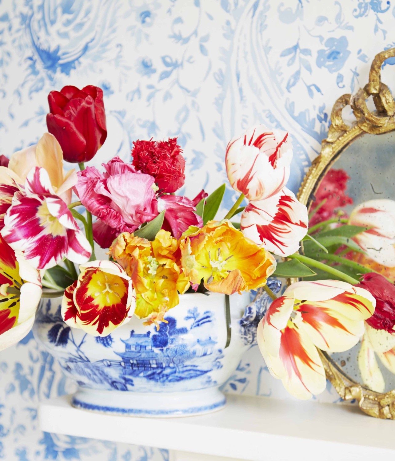 Arrangement of gold, red, pink, and striped tulips in a blue and white bowl