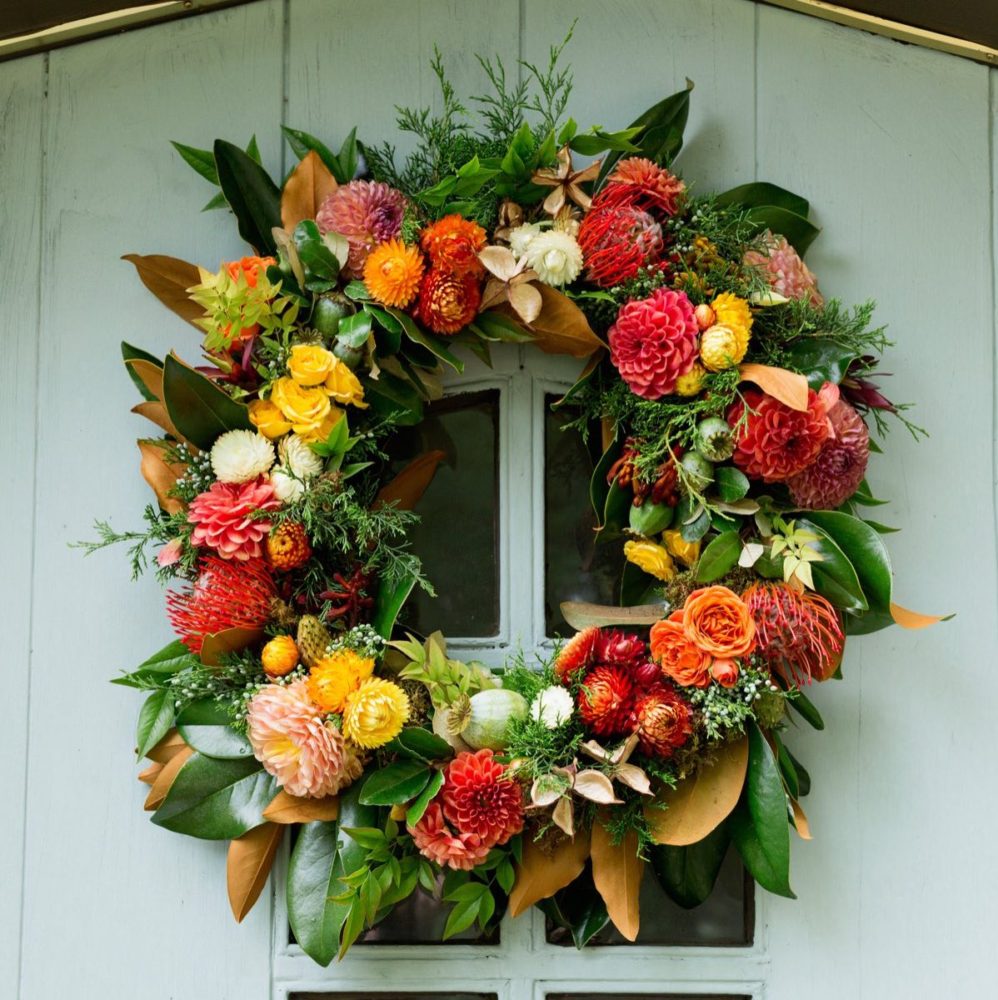 A fall wreath with dahlias hangs on a door.