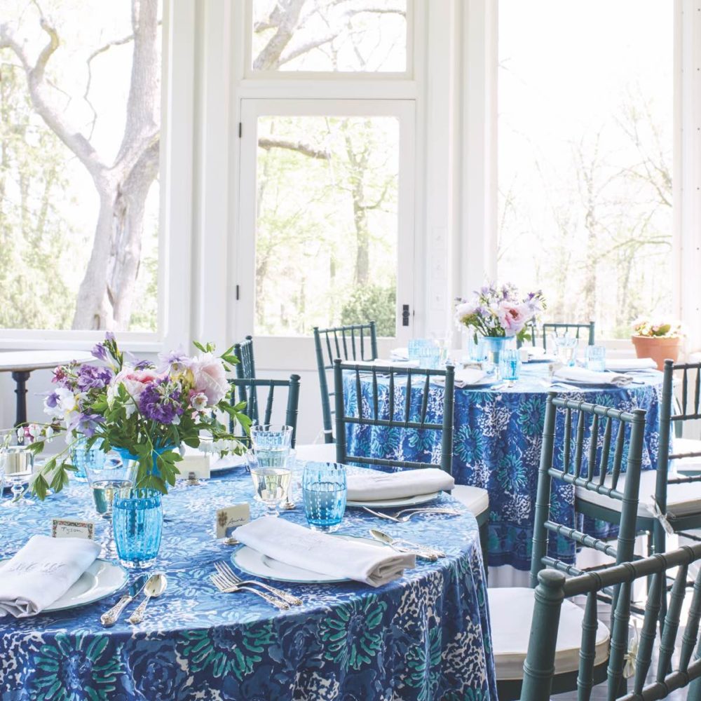 Sunroom with tables set for luncheon with blue and white tablecloths and table settings.