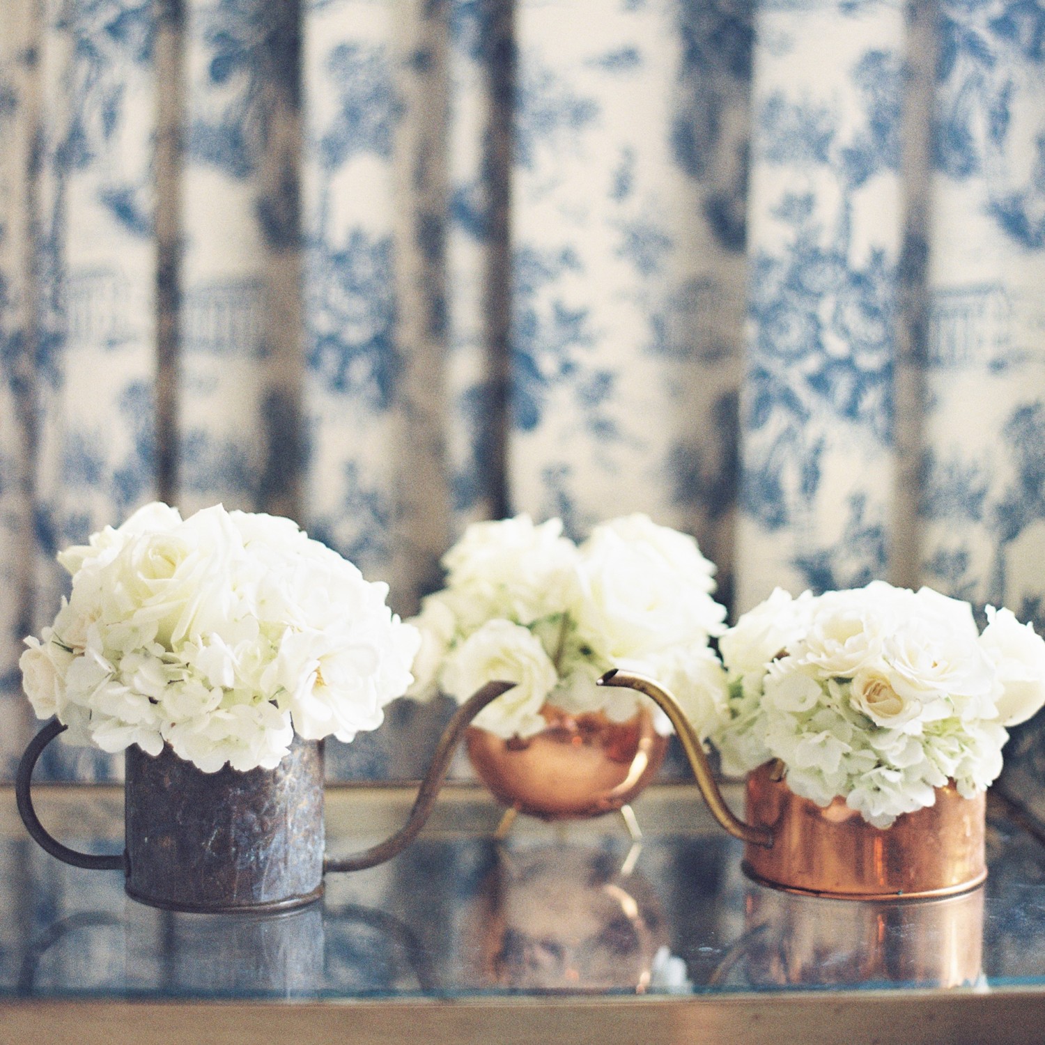 Antique copper watering cans overflow with bridesmaids bouquets of white roses and hydrangeas.