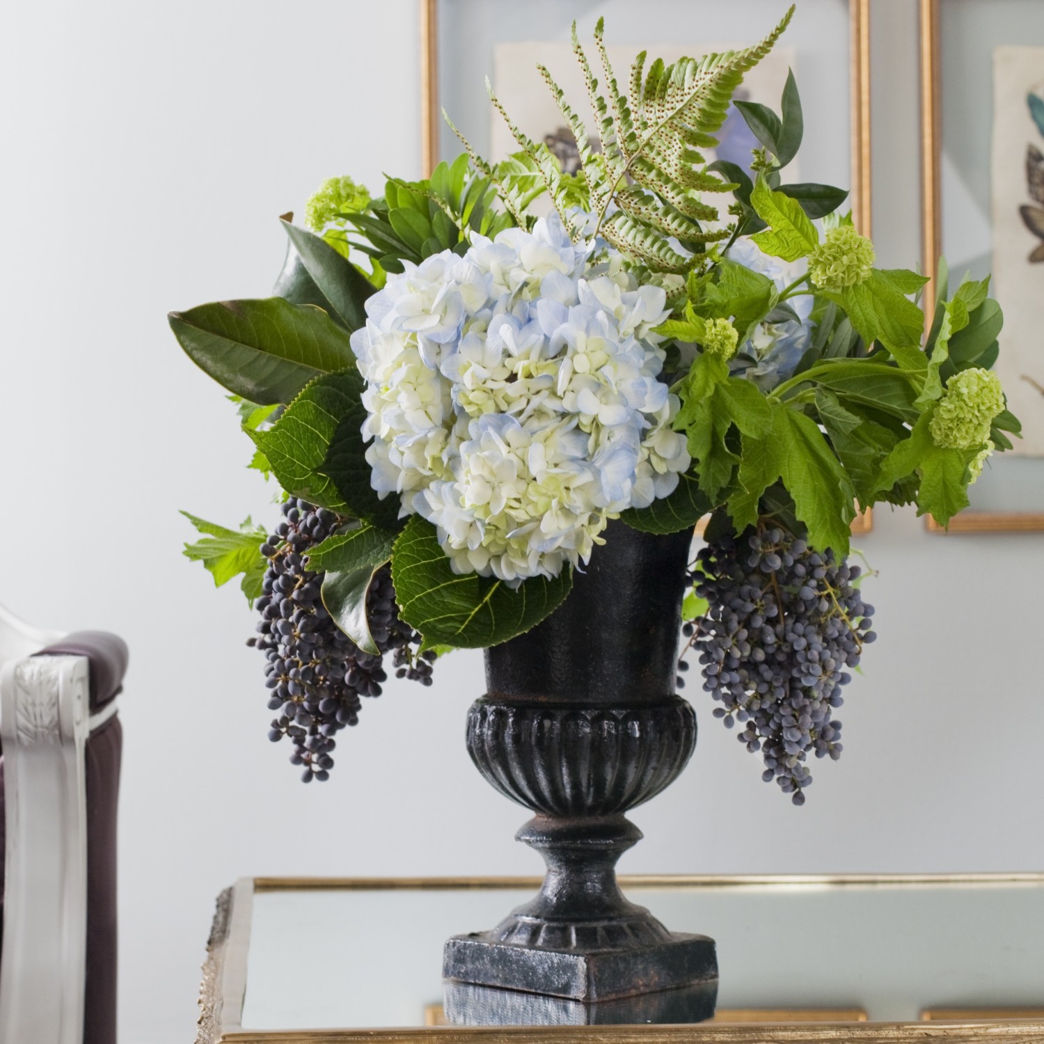 Footed metal urn filled with pale blue hydrangeas, ligustrum berries, viburnum, autumn fern, and foliage.