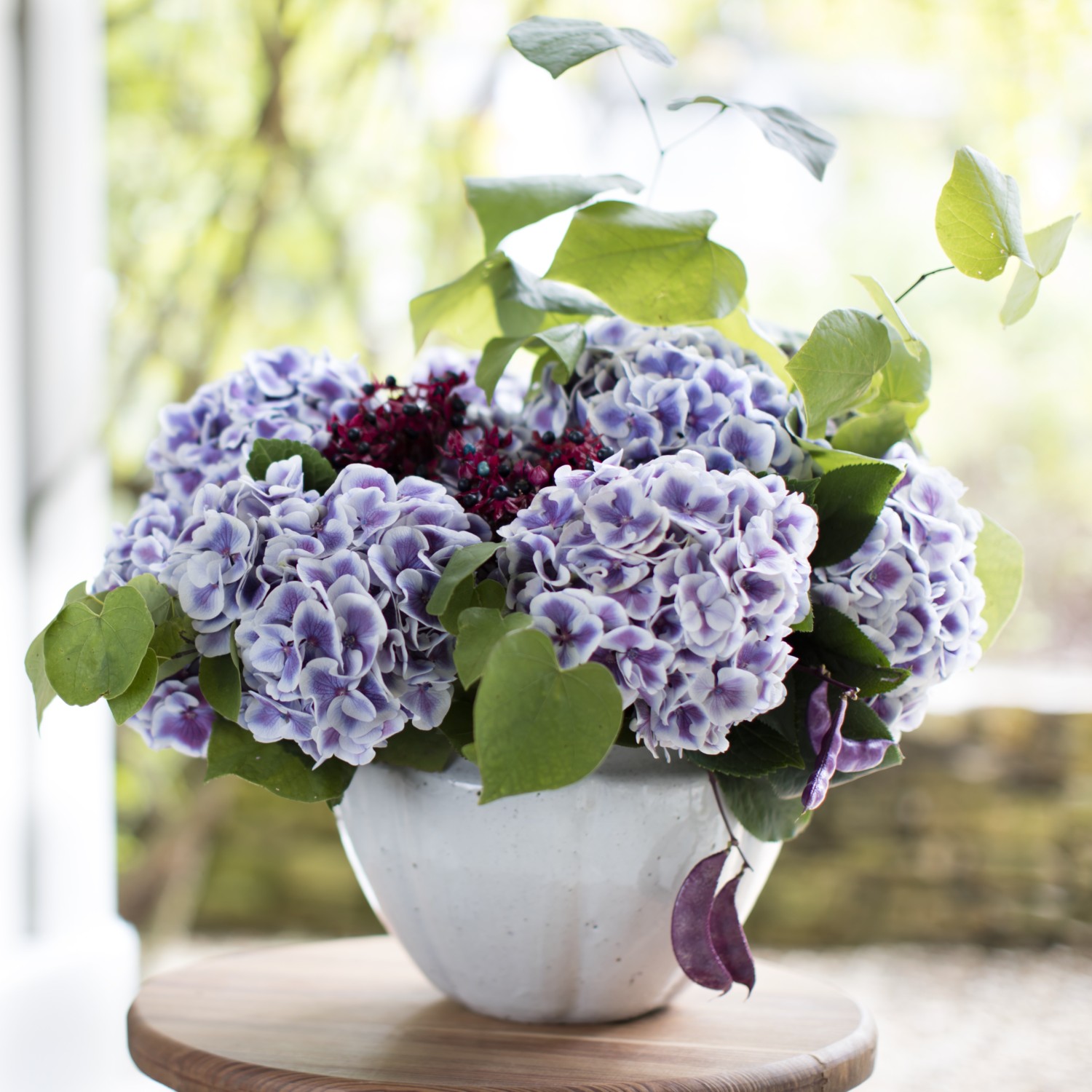 Purple washed hydrangeas and redbud leaves star in this casual summer arrangement.