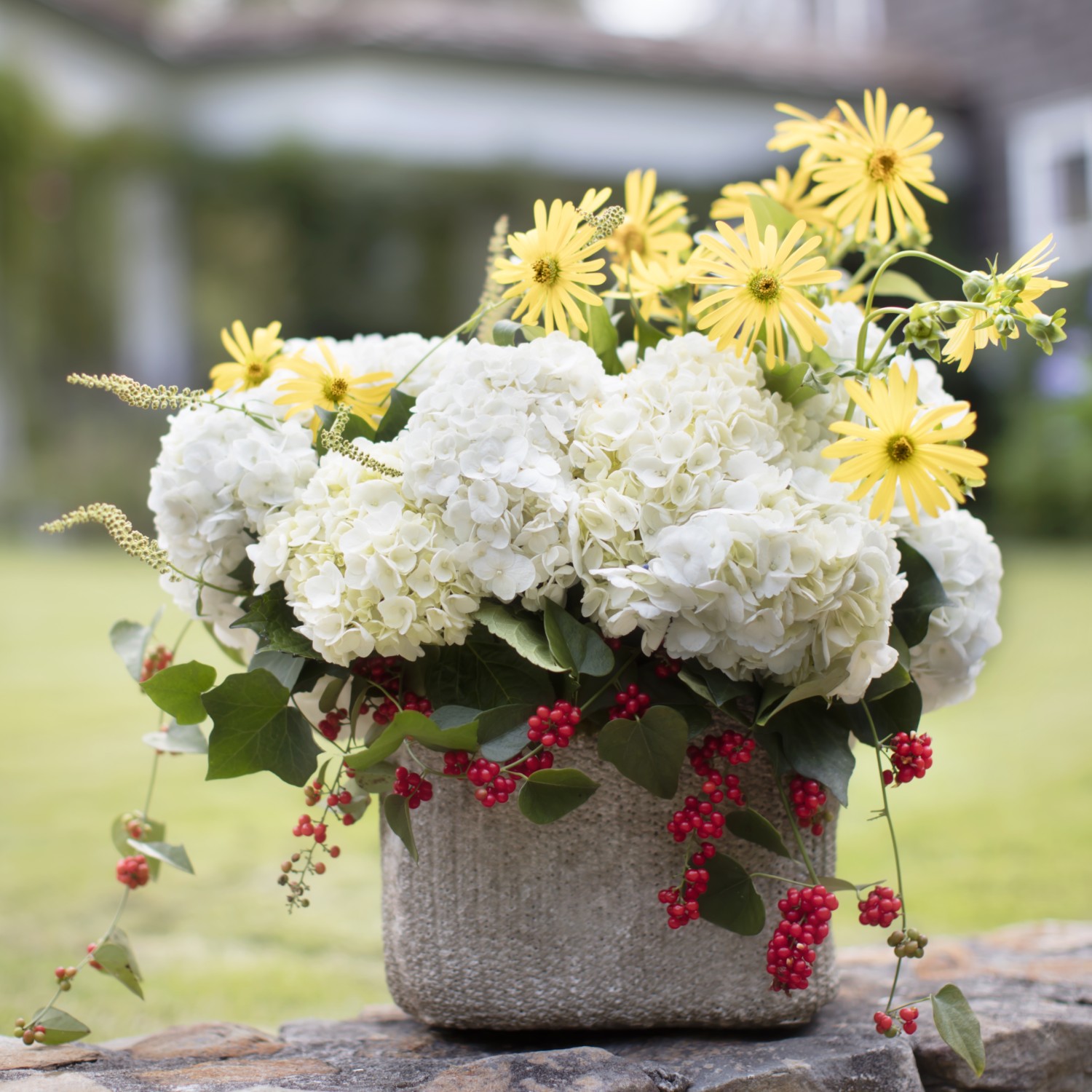 Arrangement of white hydrangea blossoms with yellow rosinweed (Silphium) flowers, and red berries.