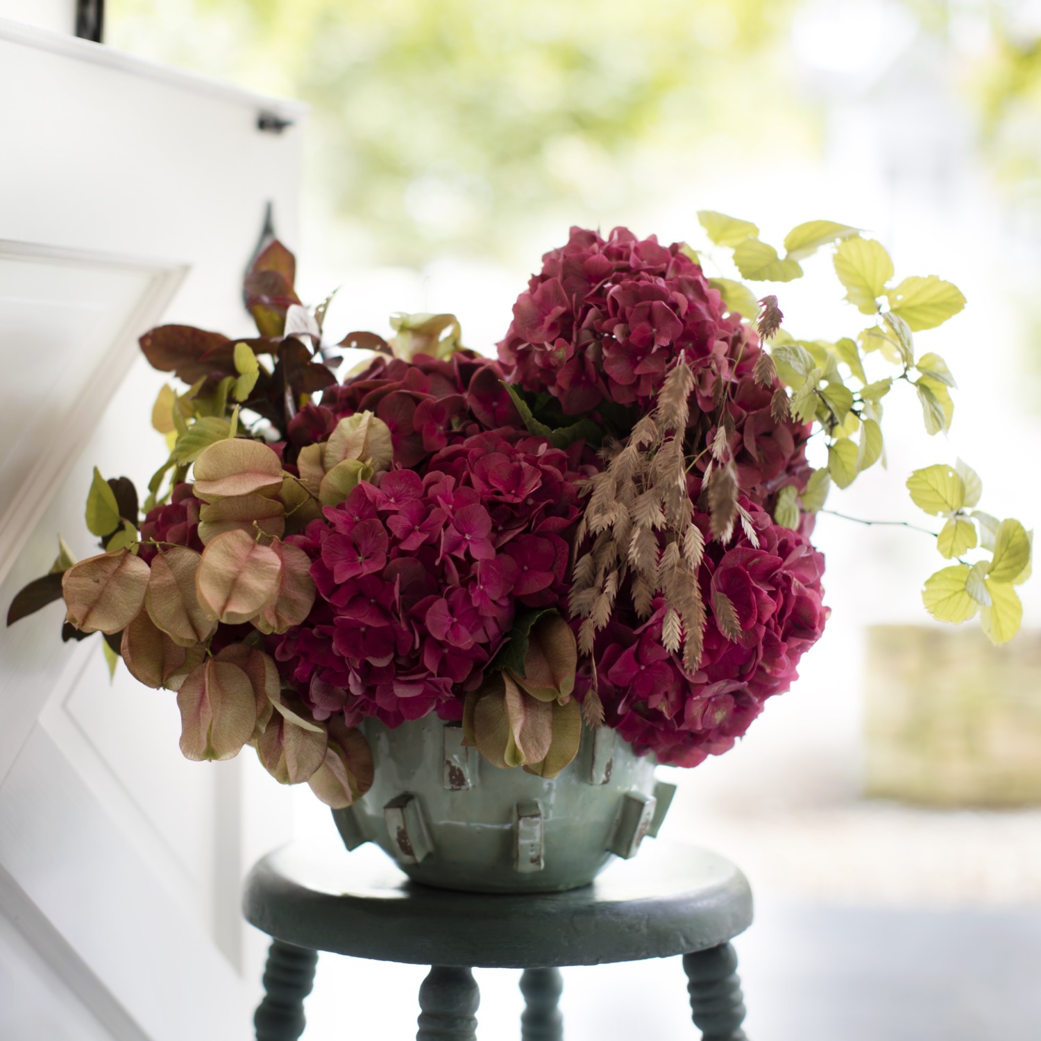 Red hydrangea blossoms blend beautifully with ruddy leaves and russet seed pods in an autumnal arrangement.