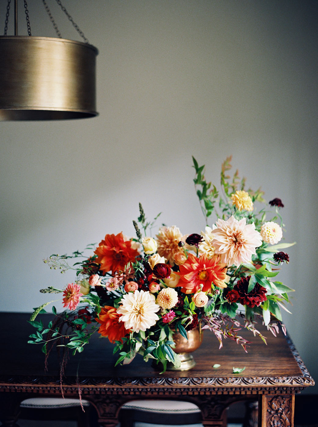 floral arrangement on an antique carved wood table beneath a cyndrical brass lamp