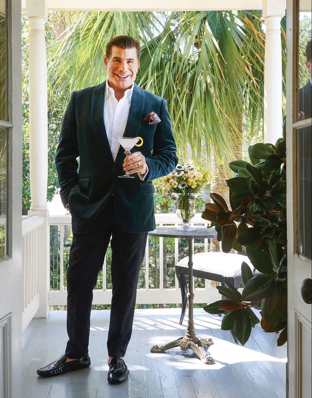 actor bryan batt stands on his covered porch, wearing a suit and holding a cocktail in a martini glass