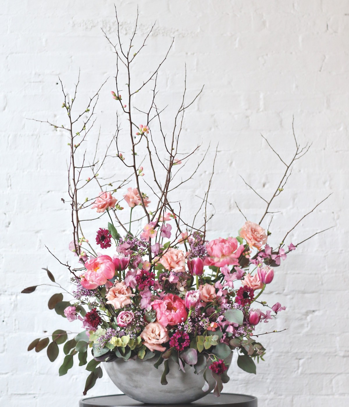 Rosy quince branches spring from a bowl full of peonies, lisianthus, fringed tulips, lilacs, sweet peas, scabiosas, and eucalyptus arranged by  Sullivan Owen.