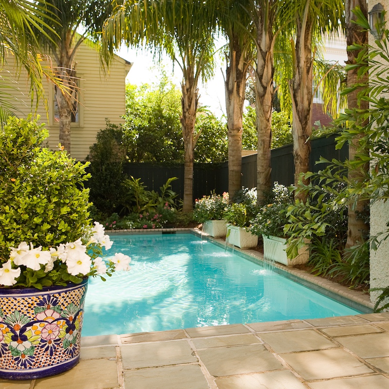Pool with Queen Palms towering overhead, poolside planters double as fountains, and mosaic containers brim with flowers and greenery.