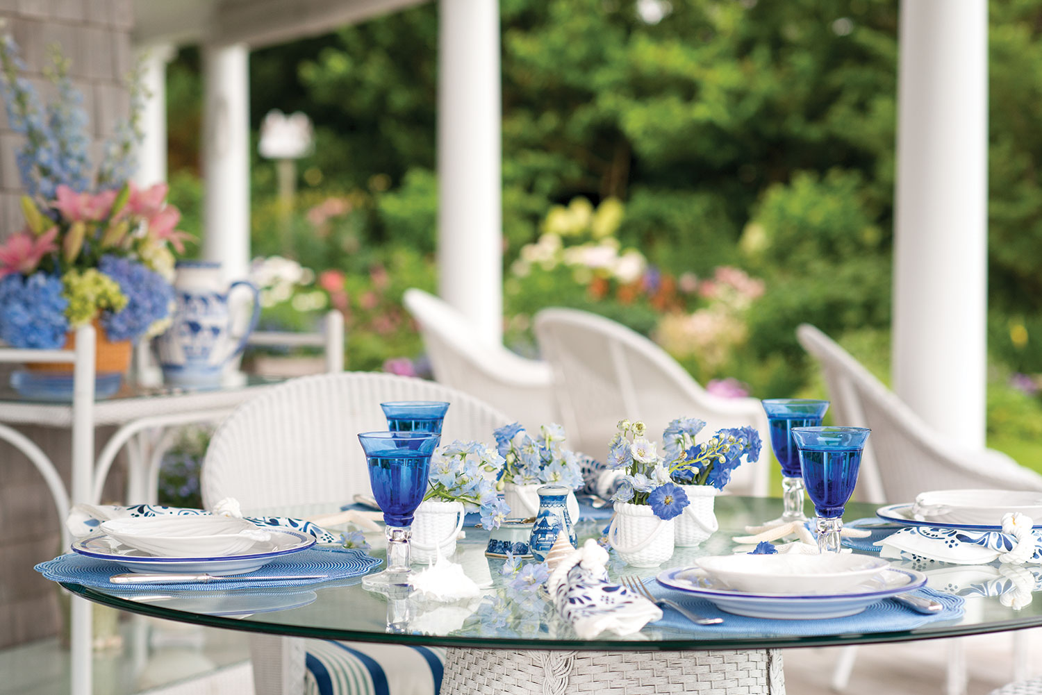 A glass table is set with blue finishes and flowers.