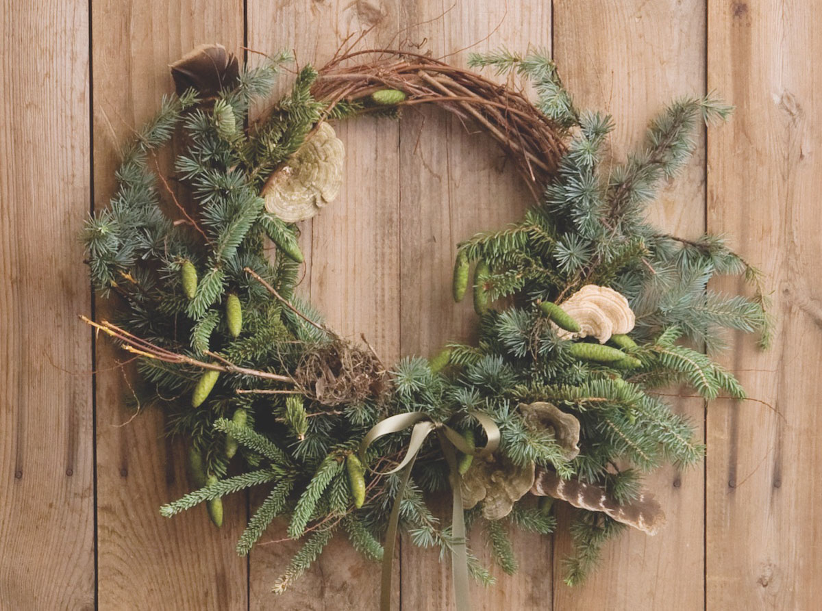 Festive Wreath by floral designer Amy Merrick featuring a grapevine form, several types of evergreen, turkey features, lichen, and a foraged bird's next