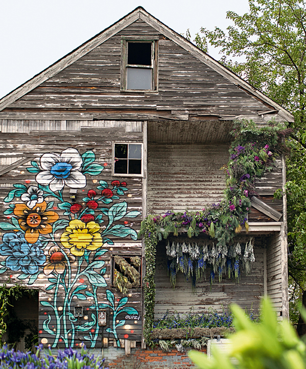 Dilapidated wood-frame house featuring a flower mural and adorned with plants
