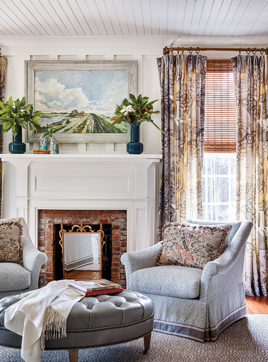 Photo of James Farmer interior design at McCurdy Plantation featuring two light blue armchairs and a round, tufted light blue leather ottoman. The walls, shiplap ceiling and mantel are all painted white.