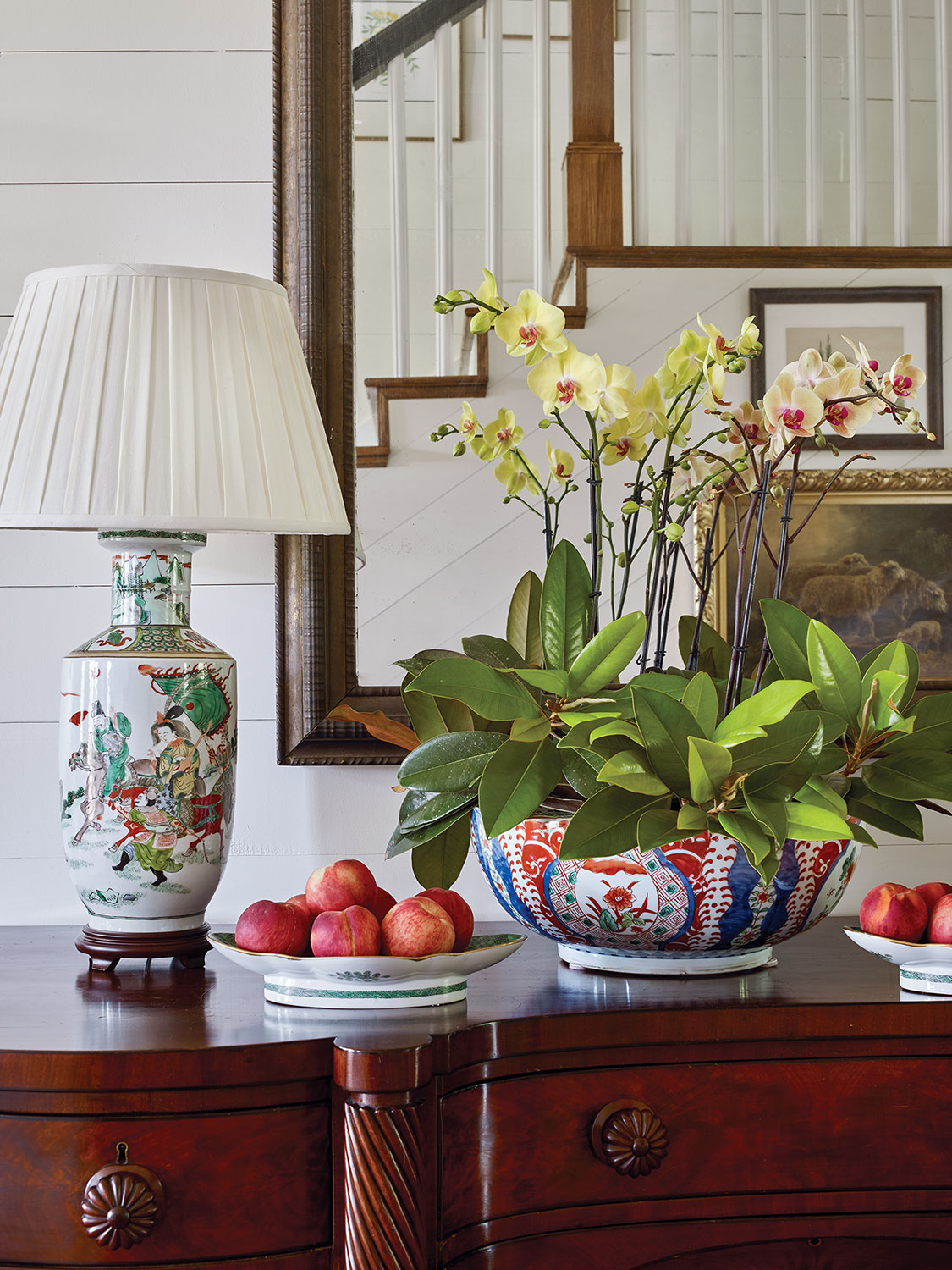 Sideboard set with lamp and large bowl filled with phalaenopsis orchids and magnolia branches.