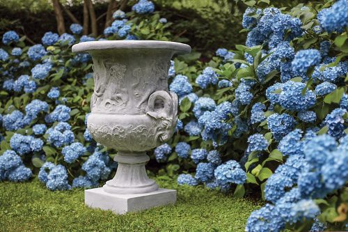 The Pennoyer Newman urn sits on a green lawn surrounded by blue hydrangeas.