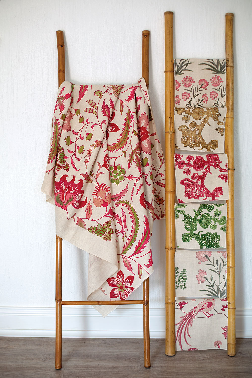 Assorted pink and green botanical print textiles, designed by Debby Tenquist of Botanica Trading, hang on bamboo display racks