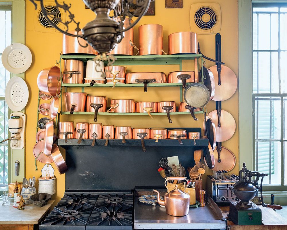 4-tier rack of copper pots above a black chef's stove with gas burners and griddle, in a Patrick Dunne's New Orleans home kitchen