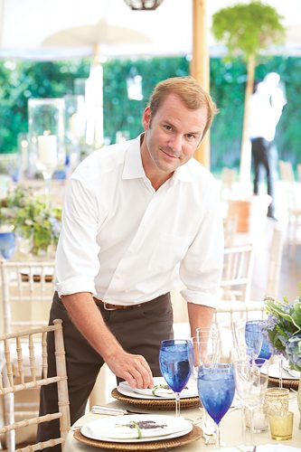 Reed McIlvaine in white button-up and black pants standing behind a table set for a party