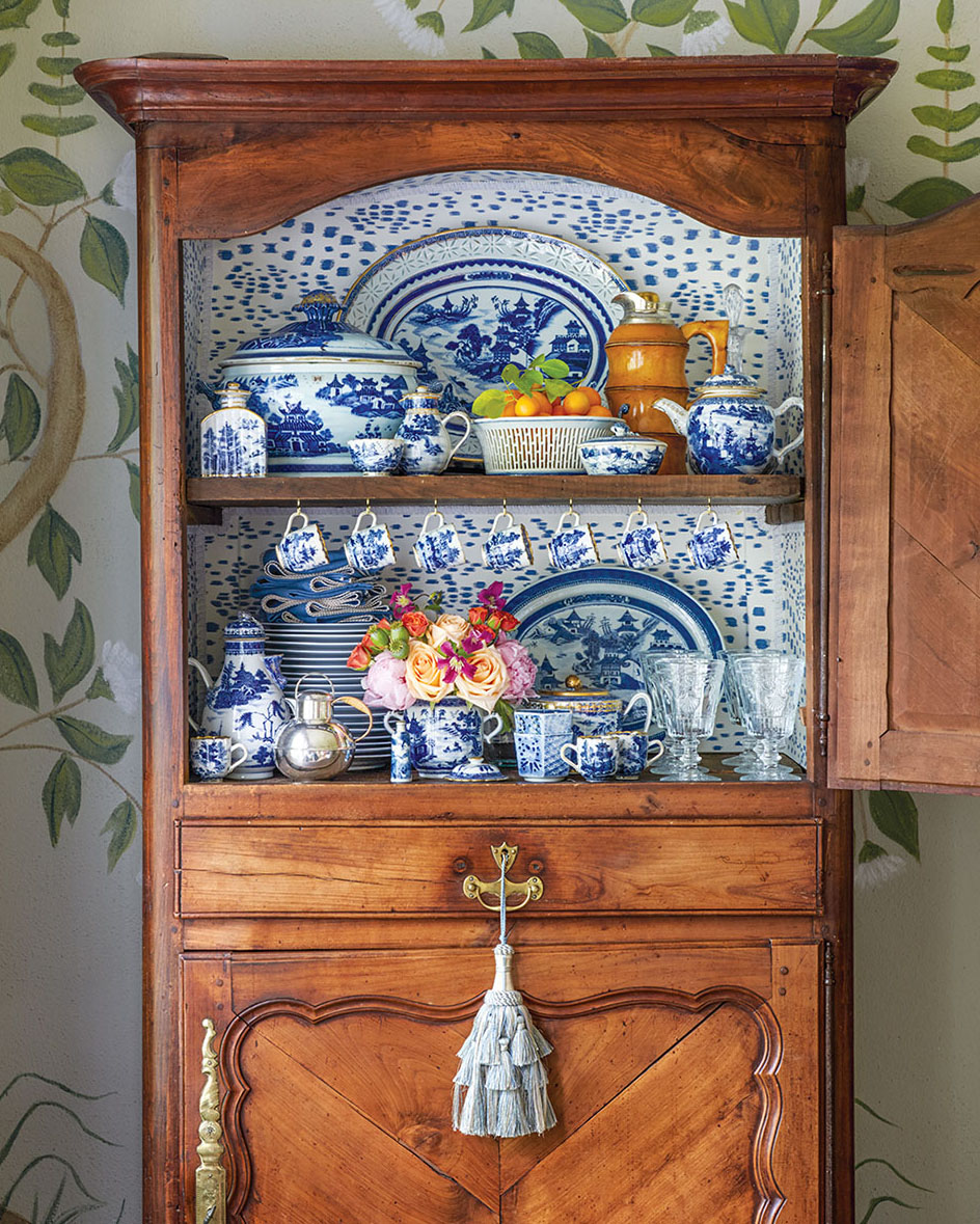 Antique wooden china cabinet, open to reveal the china inside the top half. Below, a large pale blue decorative tassel hangs from the drawer handle.