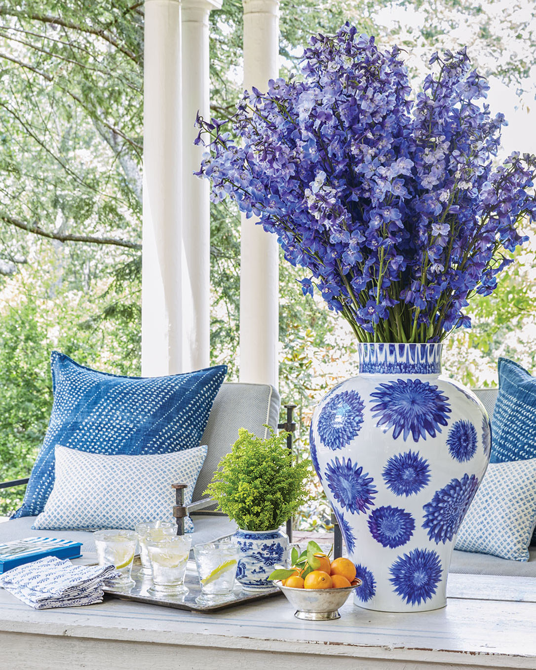 A large blue-and-white vase of blue flowers decorates a covered porch with ample seating