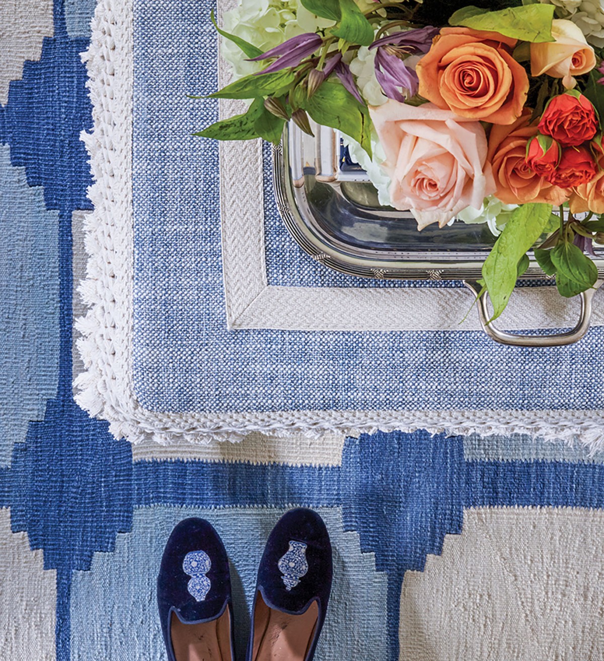 Close up of rug and bench cover with arrangement of roses, blue slippers on floor.