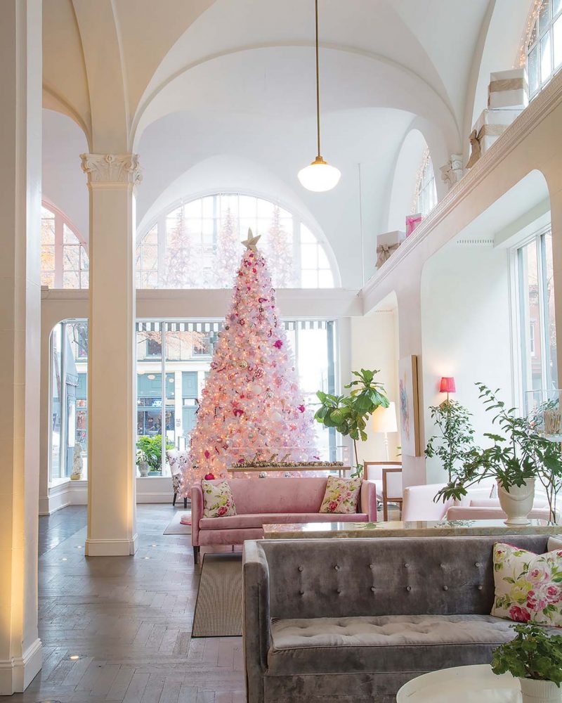 A white Christmas tree decorated with silver and red ornaments and white lights in Quirk Hotel in Richmond, Virginia. The light and airy lobby features a vaulted ceiling.