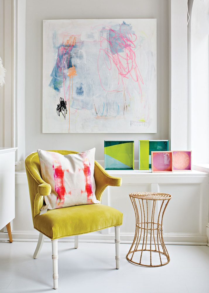 Best shopping in Richmond, Virginia: Palette Paint and Home. Photo of an avocado green velvet armchair sits next to a modern metal-base round occasional table. Bright and colorful abstract art punctuates the white room. 