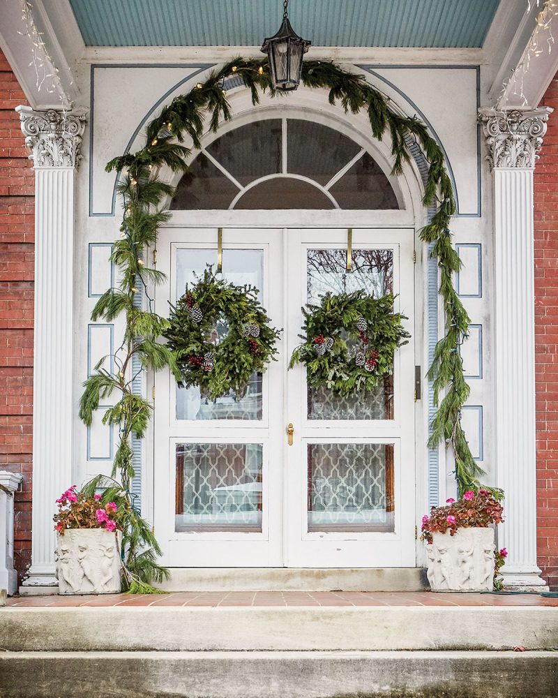 The front entry of a historic home on Monument Avenue, in Richmond, Virginia, features a holiday garland over the arched doorway, and a wreath on each side of the double door. 