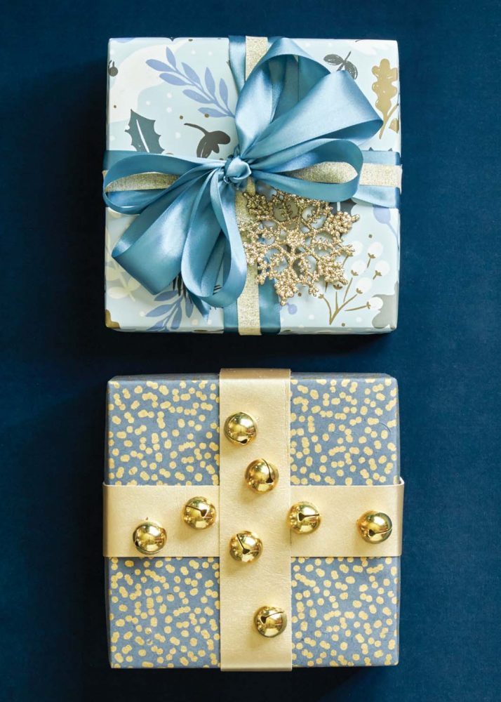 Holiday gift wrap ideas with blue and gold, and jingle bell balls attached to criss-crossed gold ribbon