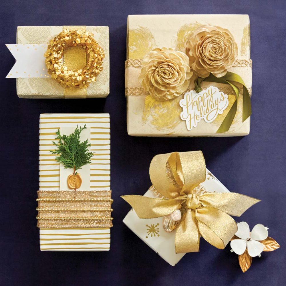 Presents wrapped in gold-and-cream colored paper. Adornments include a small golden wreath, golden rosettes, a small golden acorn ornatment, and a spring of greenery adhered with a wax seal
