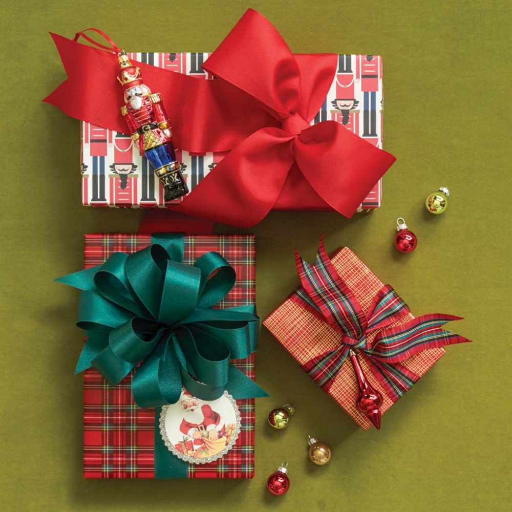 One present is wrapped in a graphic Nutcracker print, with a wide red bow and a Nutcracker ornament. A another is wrapped in a tradition red and green plaid with a deep green bow and a vintage-looking Santa Tag. The third is wrapped in red paper with crisscrossed gold times, plaid ribbon, and a red ornament