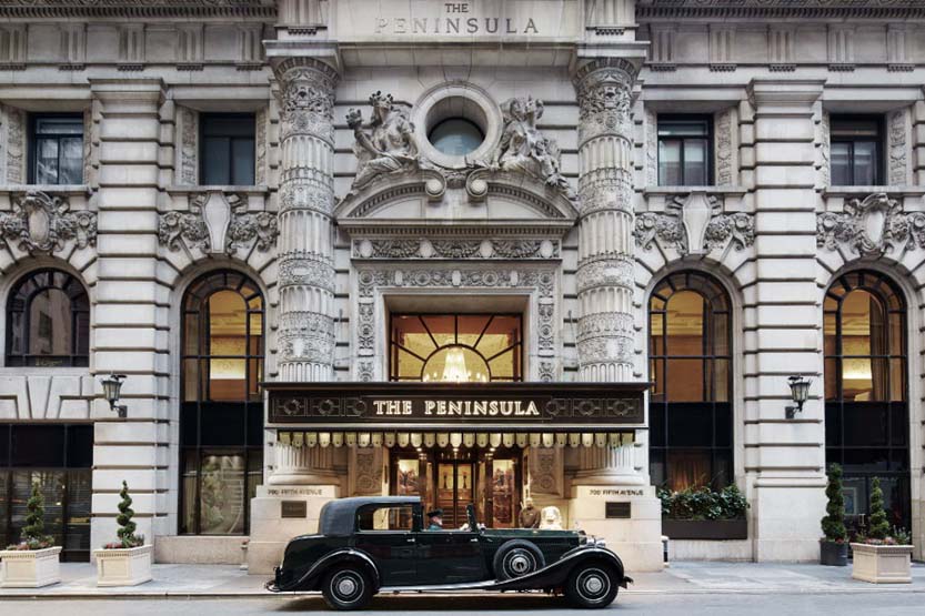 Vew of Peninsula Hotel New York's ornate facade, with a class Rolls Royce parked in front