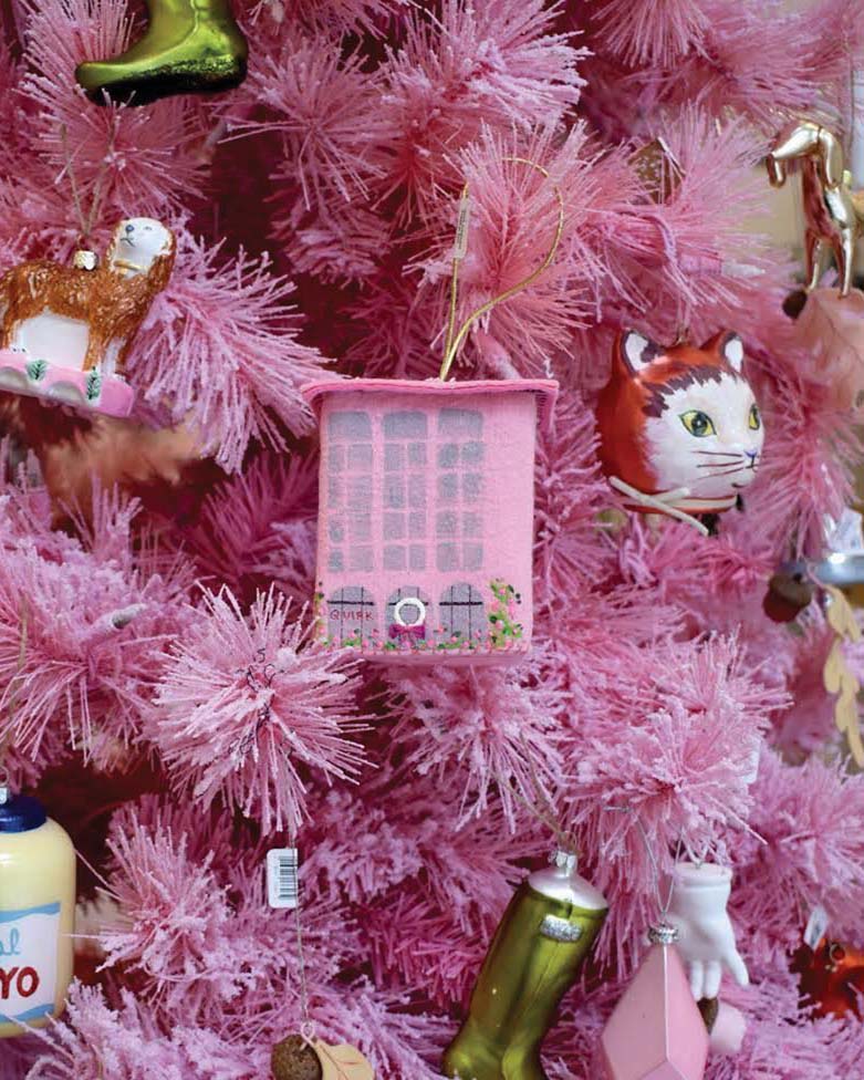 Close-up of ornaments on a pink Christmas trees, including a small building ornament by Heather Donohue and vintage-looking blown glass ornaments depicting a holiday stocking, a cat, and a dog, among others.