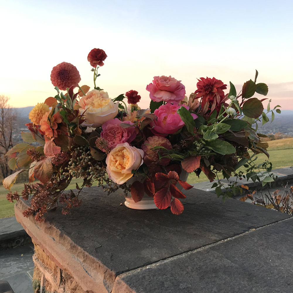 Flower arrangement set on a stone wall, with a scenic vista in the background. 