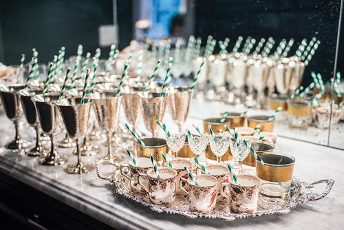 Green and white striped paper straws stand in silver goblets, stemmed crystal, and fine china mugs, which are lined up on a stone counter waiting to be filled with Brandy Freezes