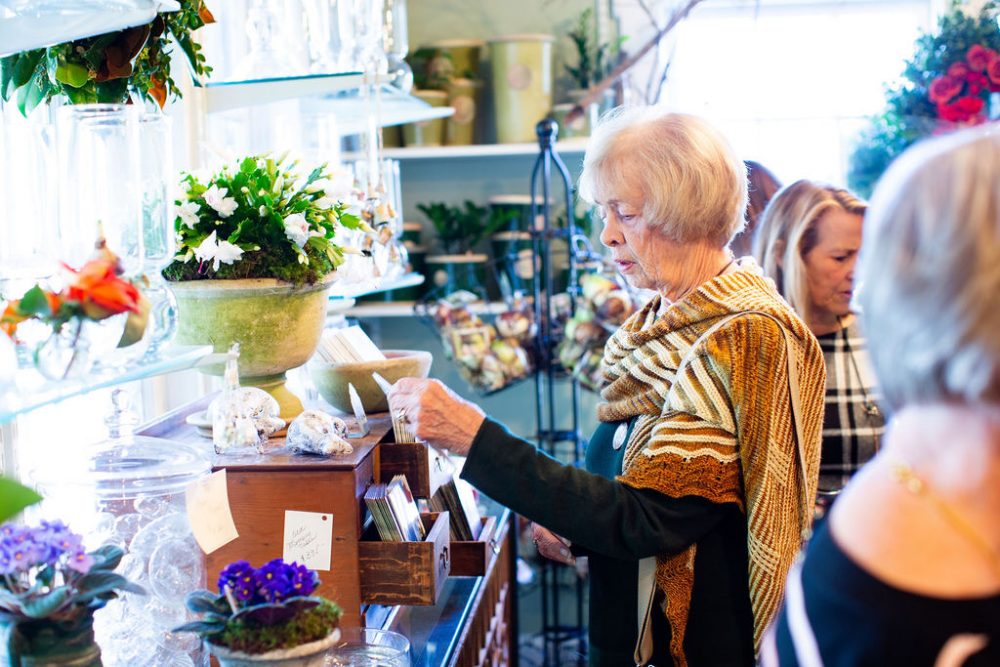 A guest at the open house peruses the gift selection at The Gardener's Cottage in Asheville, NC. Among the gifts are ample potted flowering plants and colorful blooms in vases.