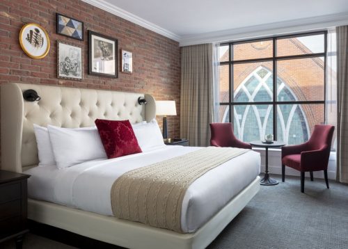 Best hotels in Asheville: A room at The Foundry, featuring exposed brick walls and a view looking onto a large stained glass window of a church in downtown Asheville