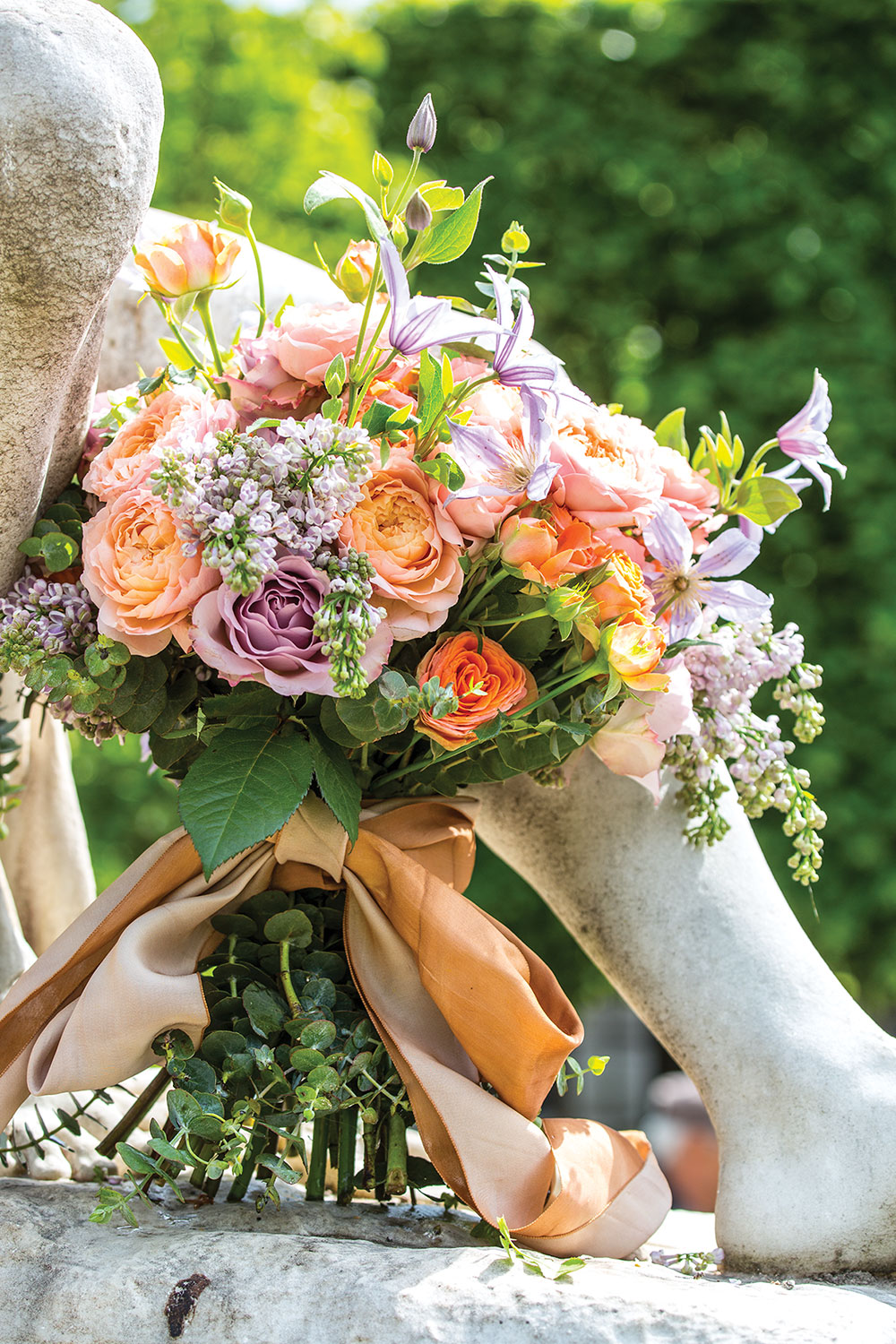 French bouquet of roses and clematis with orange ribbon on sculpture