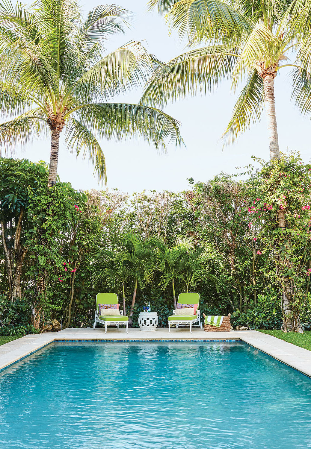 Pool flanked by palm trees with pair of lounges at end.
