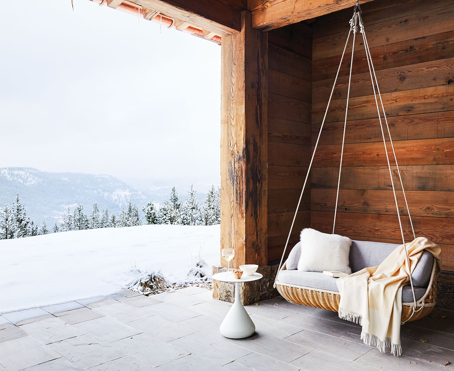 A cozy hanging seat on the deck looking over a snow covered mountain.