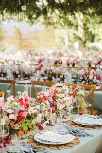 Red, white, and pale pink flowers sit nestled on a table with bright lime colored greenery. Blue patterned plates with menus on top sit next to the overflowing flowers.