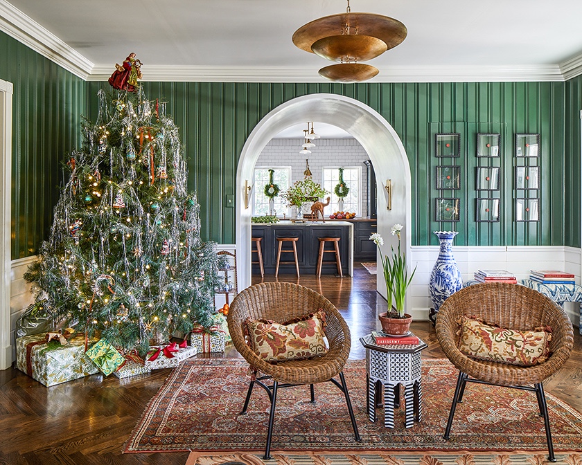 A Christmas tree covered in silver tinsel lights up the corner of a green paneled room.