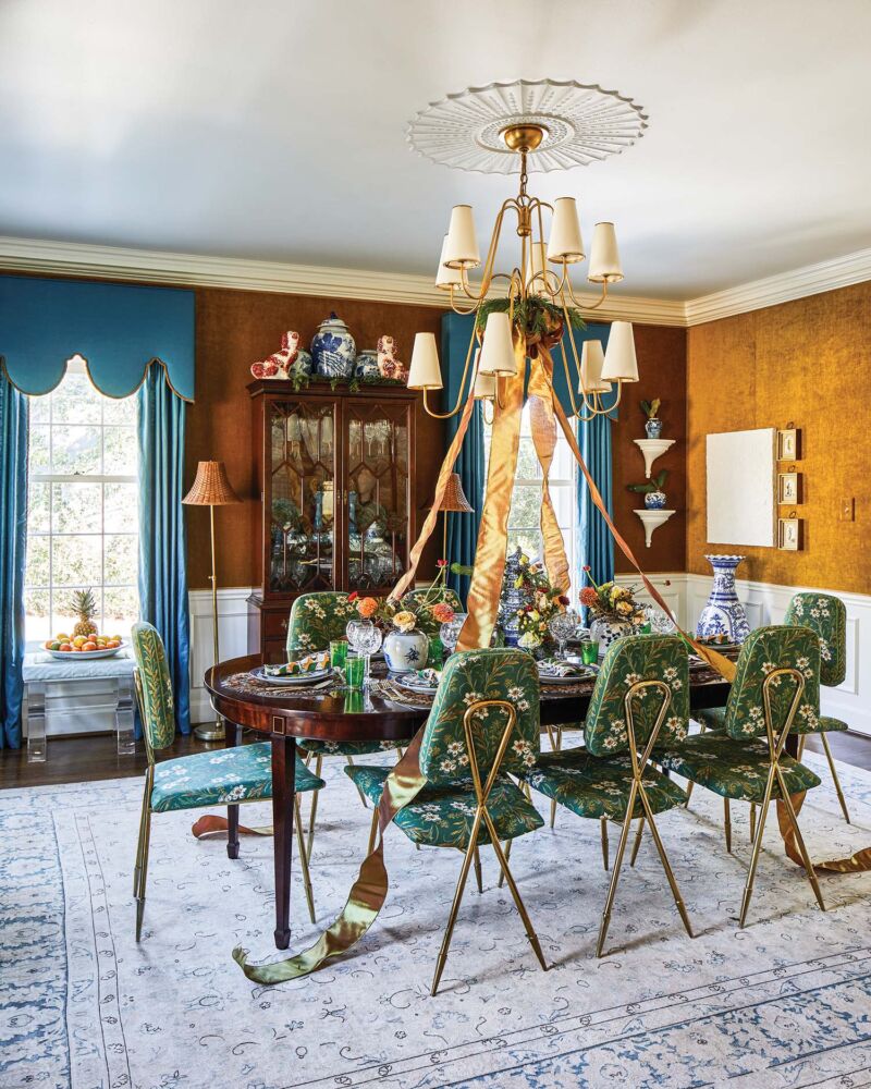 Dining room with turquoise drapery, tobacco-colored walls, green floral prints on dining chairs and gold ribbon and holiday greenery on the chandelier.