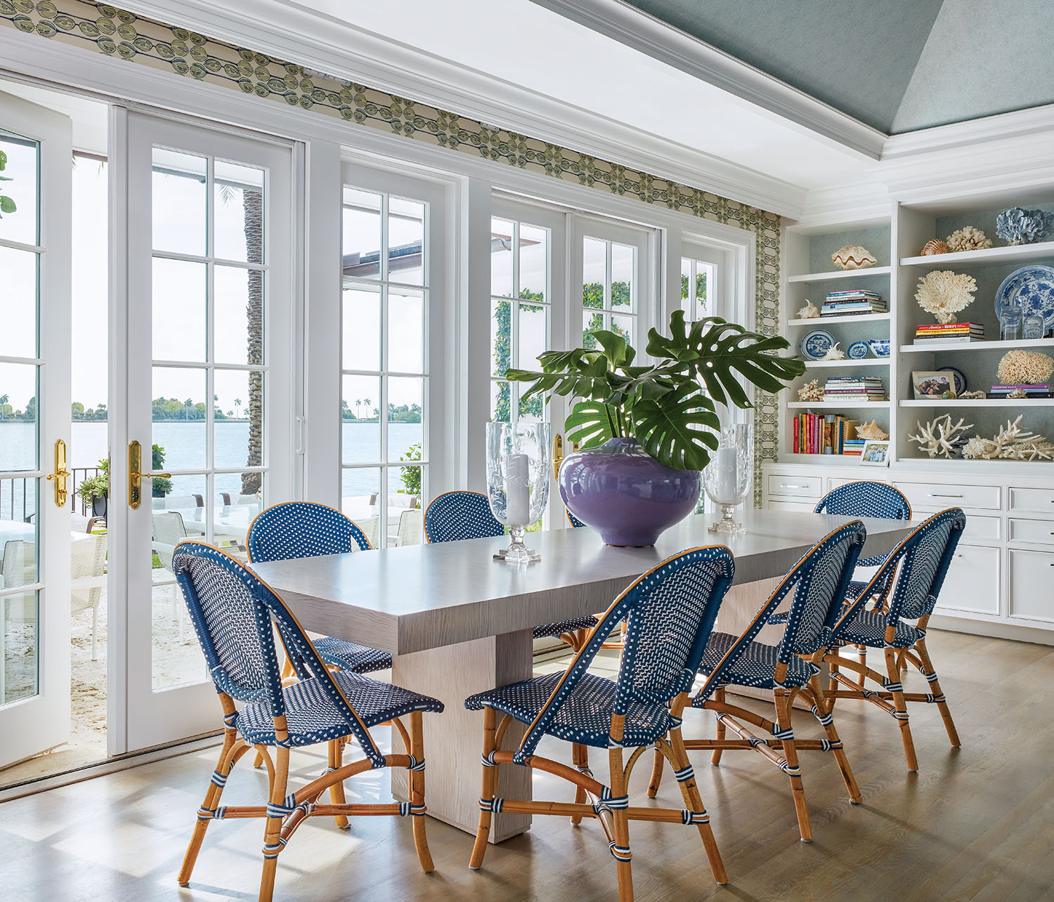 Blue dining chairs around a white table in front of french doors.